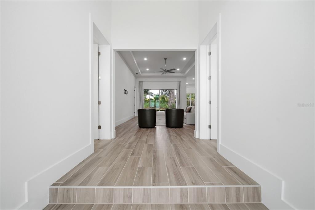 A hallway with wood-look tile flooring leads to a living area with a tray ceiling — 555 SANCTUARY GOLF PLACE, APOPKA, FL