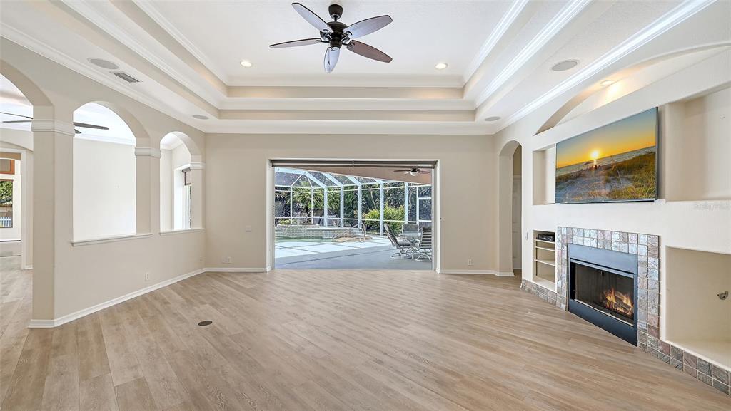 A living room with a tray ceiling, fireplace, built-in shelving, and sliding doors to a pool — 13112 PEREGRIN CIRCLE, BRADENTON, FL