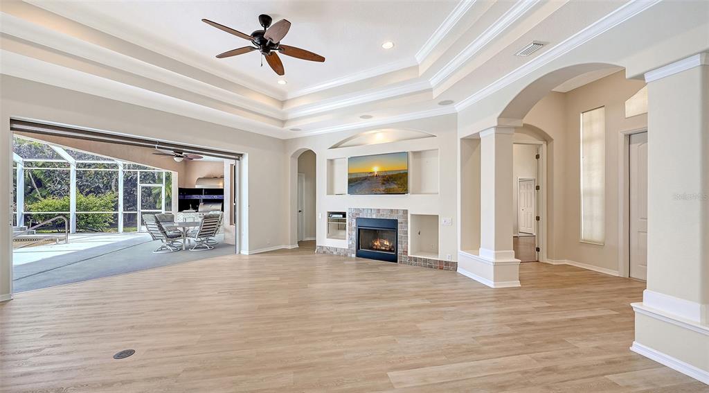 A spacious living room features light wood flooring, a fireplace, built-in shelving, and sliding glass doors — 13112 PEREGRIN CIRCLE, BRADENTON, FL