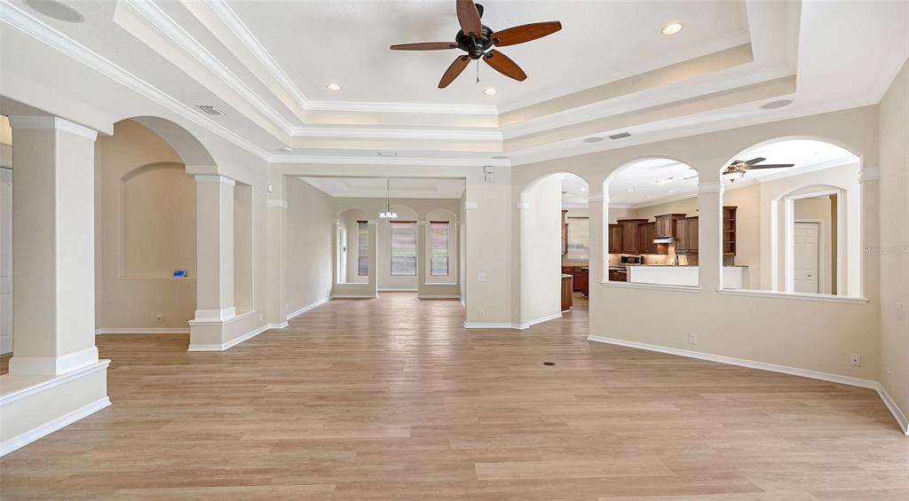 An open-concept living area features light wood-look flooring, a tray ceiling, and arched wall openings — 13112 PEREGRIN CIRCLE, BRADENTON, FL
