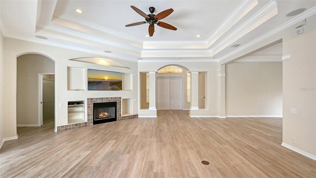 A spacious living room features a tray ceiling, a fireplace, and light wood-look flooring — 13112 PEREGRIN CIRCLE, BRADENTON, FL