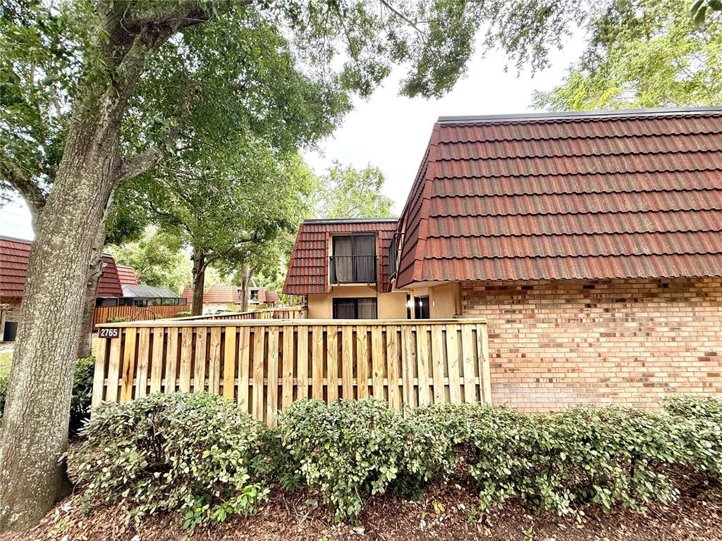 A brick townhouse exterior features a wooden privacy fence and a dark shingled mansard roof — 2747 5TH CT, PALM HARBOR, FL