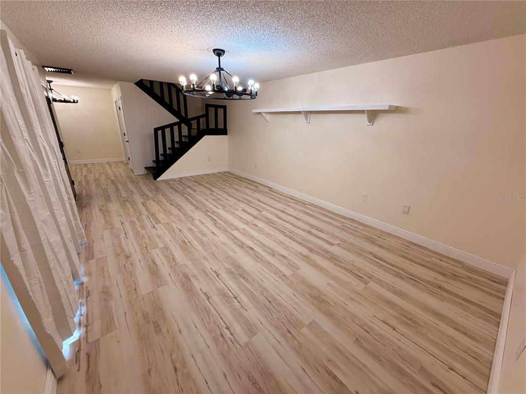An empty room features light wood-look flooring, a black chandelier, and a floating wall shelf — 2747 5TH CT, PALM HARBOR, FL