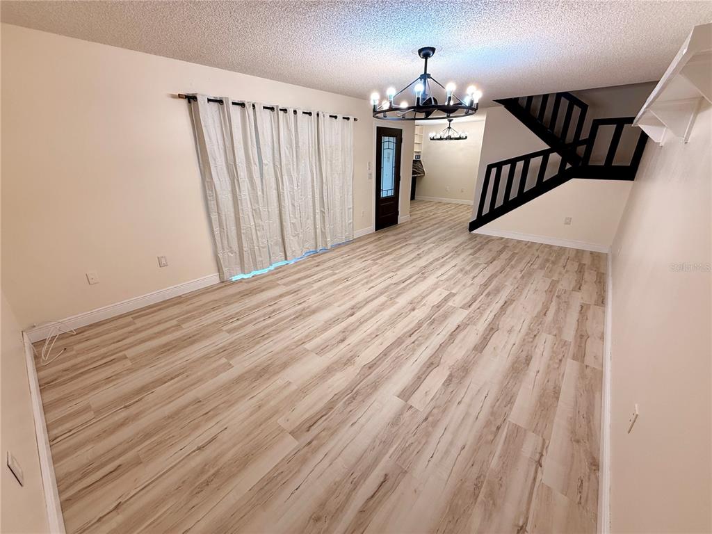 A living room features light wood-look flooring, a dark staircase, and a large chandelier — 2747 5TH CT, PALM HARBOR, FL