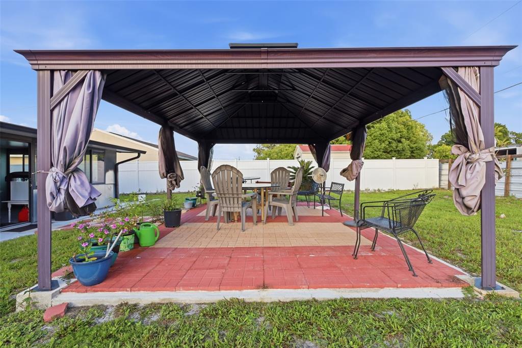 A metal gazebo with curtains sits over a red and tan paver patio in a yard — 2287 BELEN DRIVE, DELTONA, FL