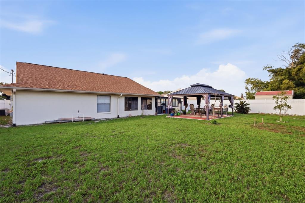 A backyard features a house with a tan roof, a gazebo, and a white fence — 2287 BELEN DRIVE, DELTONA, FL