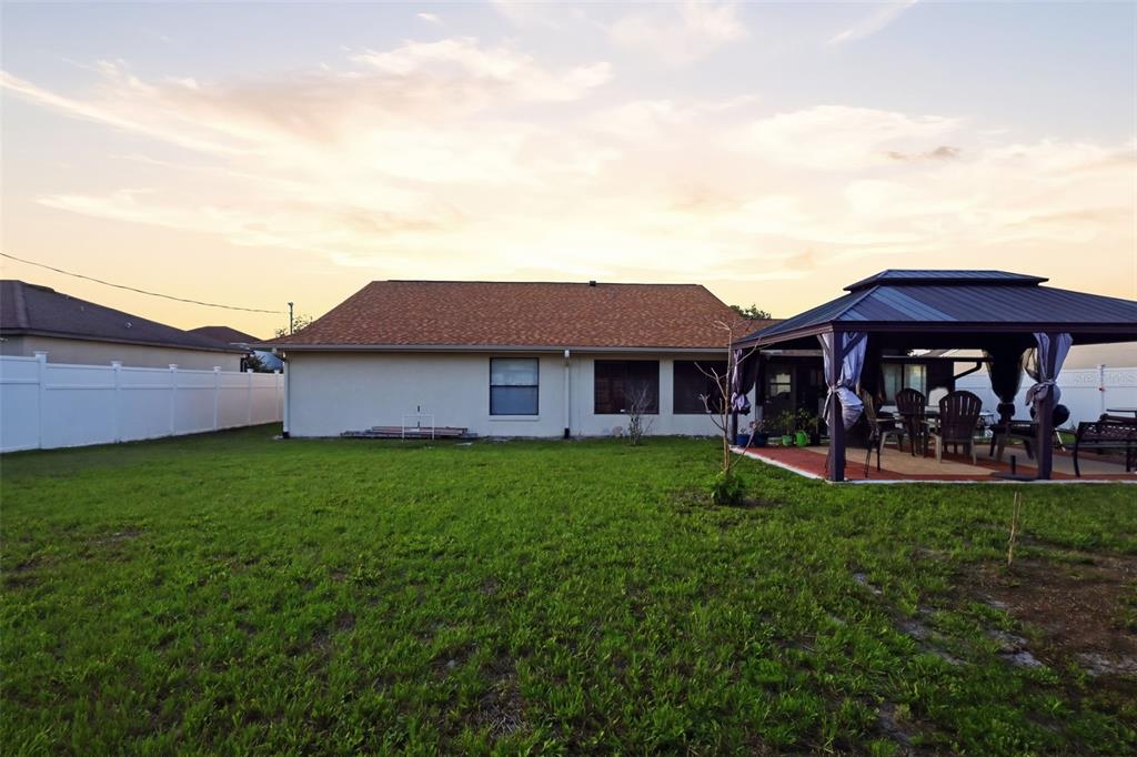 A backyard view of a house with a white fence and a metal gazebo — 2287 BELEN DRIVE, DELTONA, FL