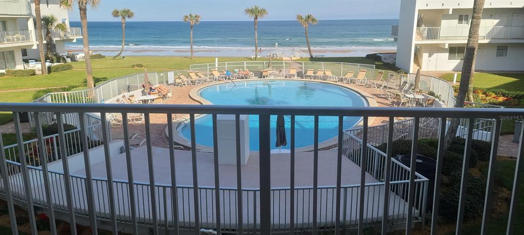 A balcony view overlooks a swimming pool, grassy lawn, and the ocean beyond — 815 OCEAN SHORE BOULEVARD UNIT 7A, ORMOND BEACH, FL