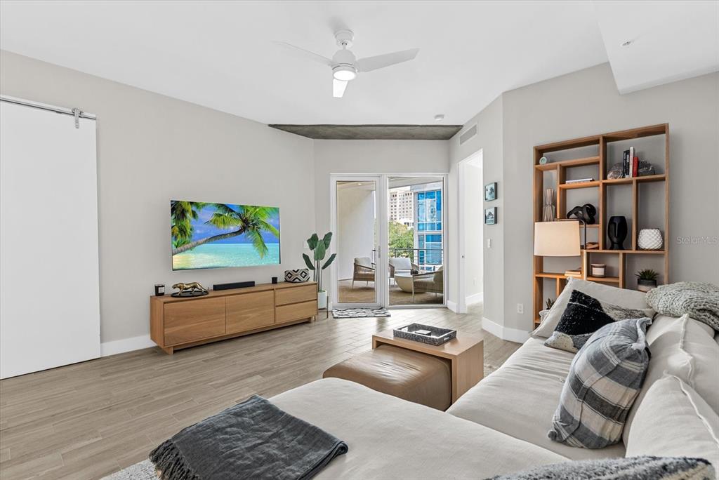 A modern living room features a sectional sofa, media console, shelving unit, and balcony access — 332 COCOANUT AVENUE UNIT 302, SARASOTA, FL