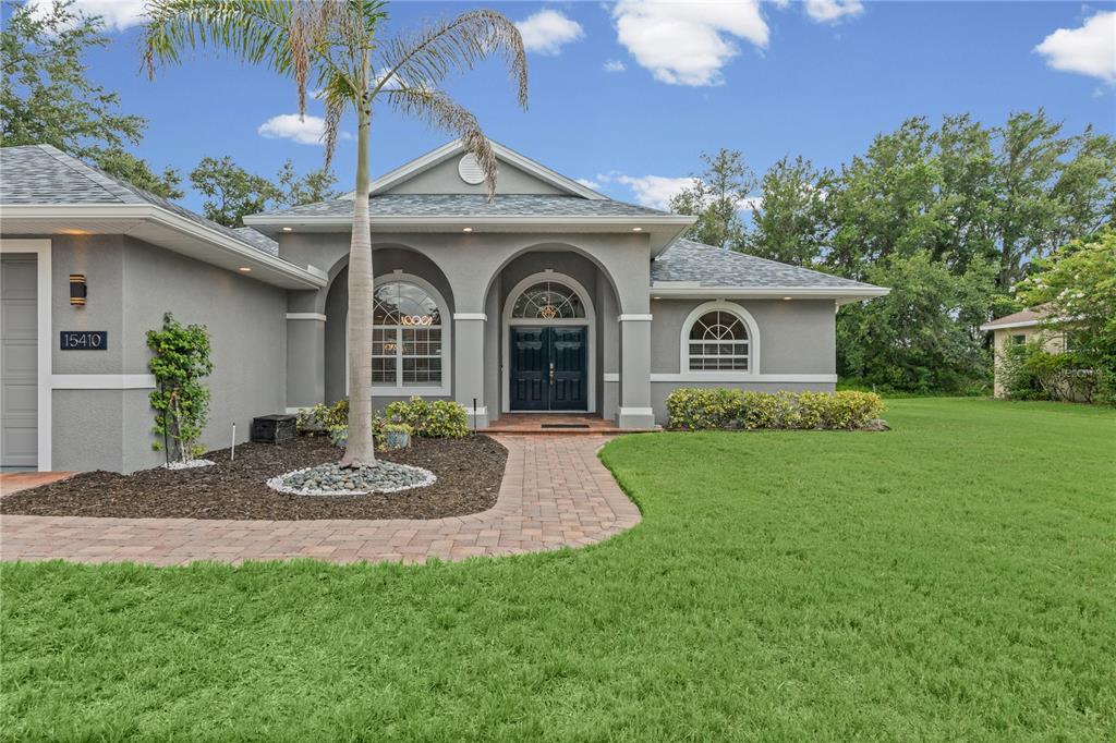A gray single-story house features a paved walkway, arched entryway, and a palm tree — 15410 21ST AVENUE E, BRADENTON, FL