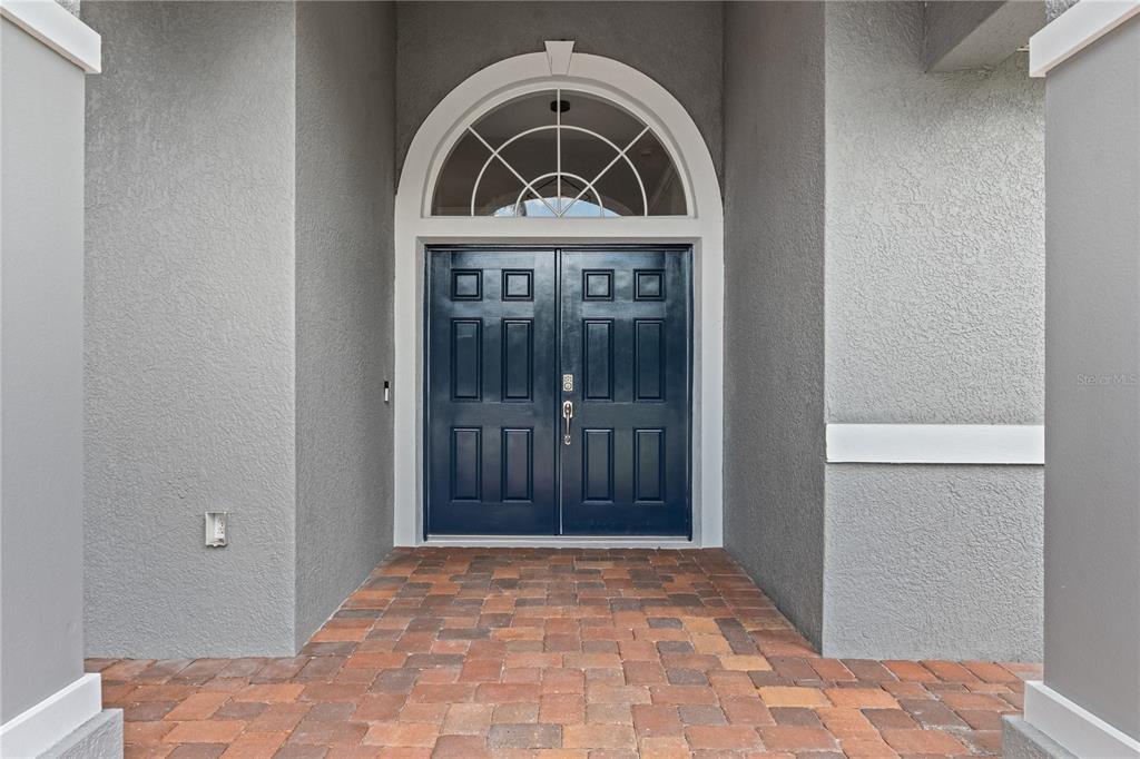 A dark blue double front door with a semi-circular transom window sits under a covered entryway — 15410 21ST AVENUE E, BRADENTON, FL