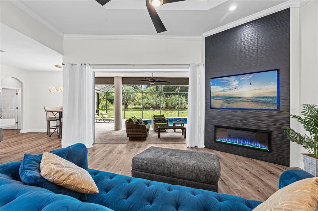A living room features a blue tufted sofa, a fireplace, and sliding doors to a pool — 15410 21ST AVENUE E, BRADENTON, FL