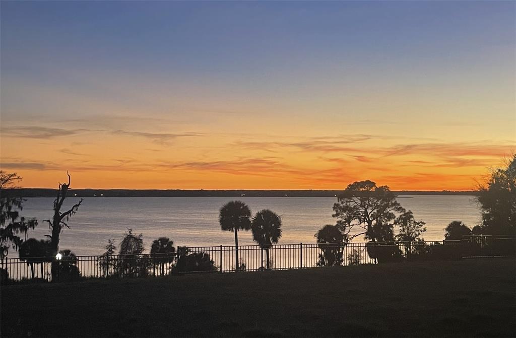 A sunset view over a lake with palm trees and a metal fence in the foreground — 624 CASEY LOOP, MOUNT DORA, FL
