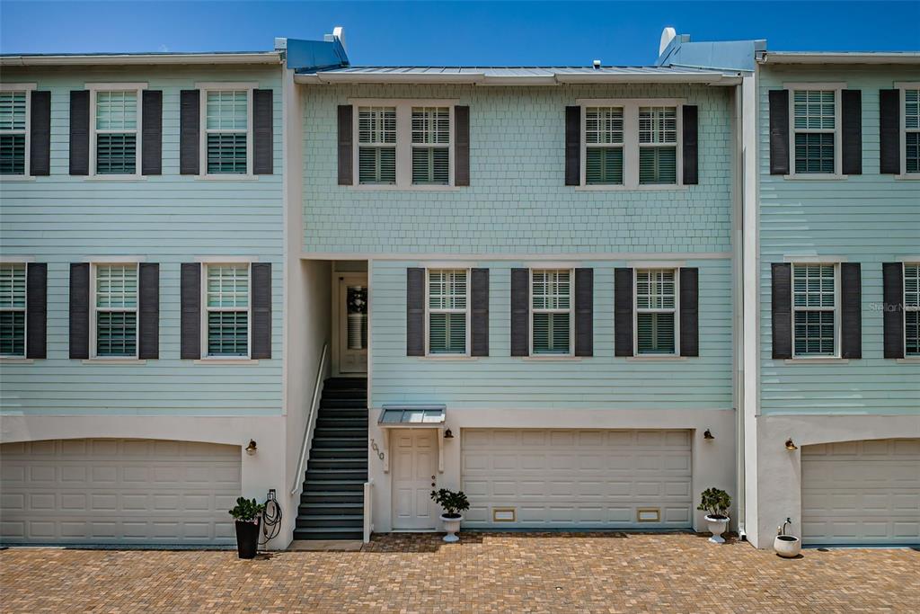 The exterior of a multi-story house features light blue siding, a paver driveway, and garages — 7010 GREVILLA AVENUE S, SOUTH PASADENA, FL