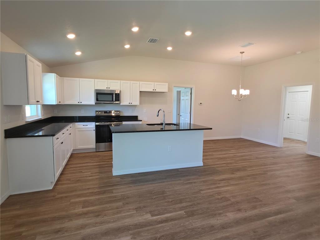 A kitchen with white cabinets, black countertops, and wood-look flooring in an open floor plan — 8270 N WAKEFIELD DRIVE, CITRUS SPRINGS, FL