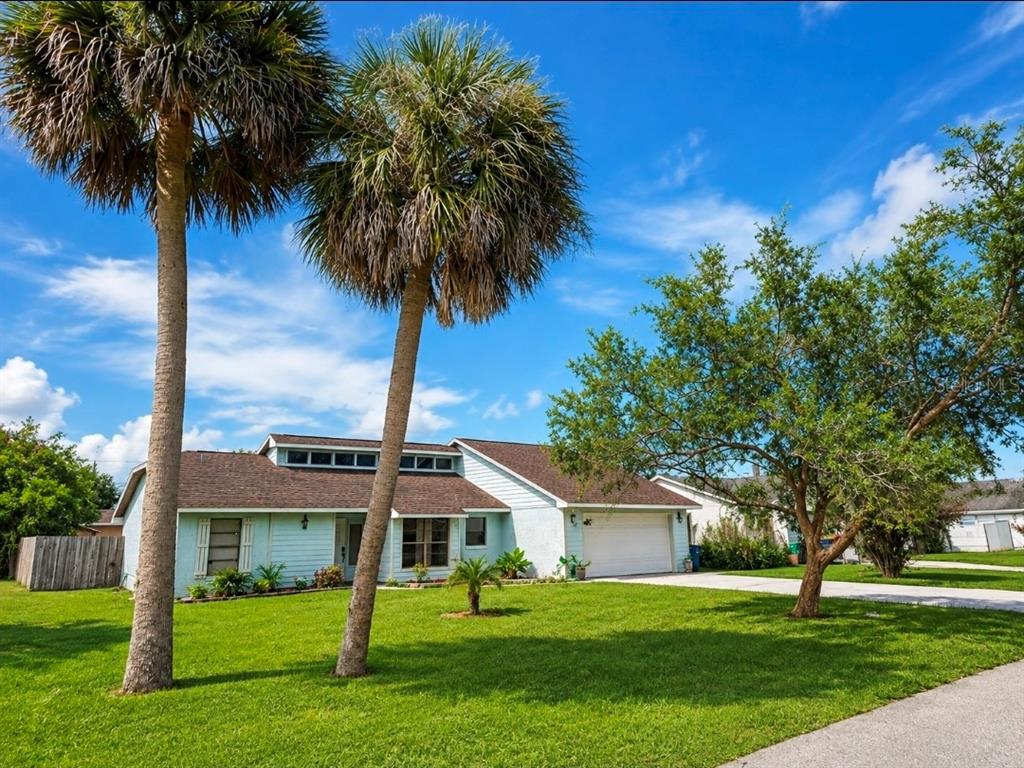 A light blue single-story house with a two-car garage and two tall palm trees — 1819 JUNIPER DRIVE, EDGEWATER, FL