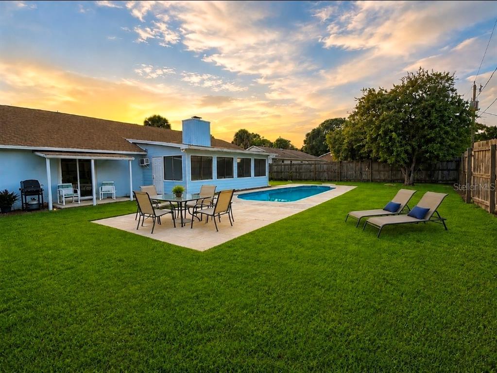 A backyard features a swimming pool, a paved patio with dining furniture, and two lounge chairs — 1819 JUNIPER DRIVE, EDGEWATER, FL