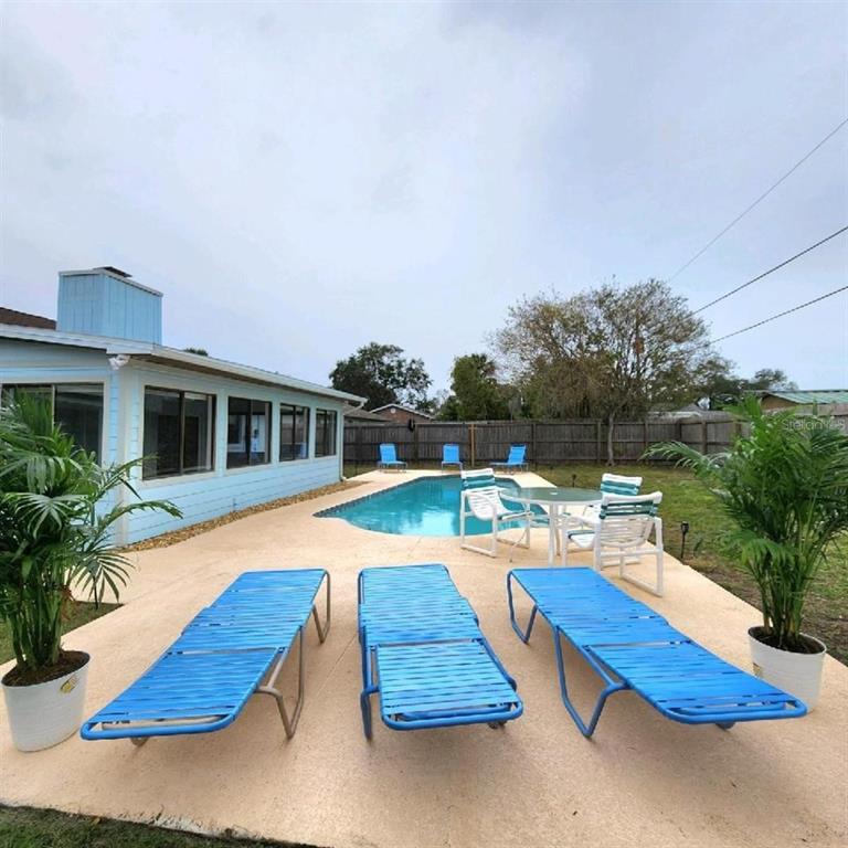 A light blue house with a sunroom and chimney overlooks a backyard swimming pool — 1819 JUNIPER DRIVE, EDGEWATER, FL