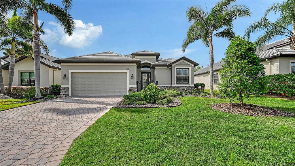 A single-story suburban house with a paved driveway, two-car garage, and palm trees — 7702 RIO BELLA PLACE, BRADENTON, FL