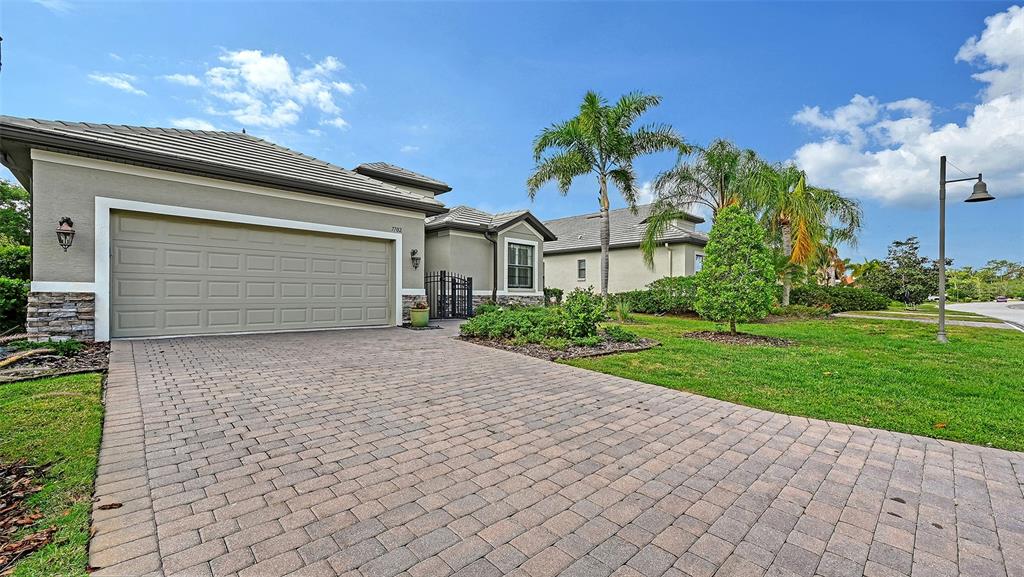 A single-story house features a paved driveway, a two-car garage, and palm trees — 7702 RIO BELLA PLACE, BRADENTON, FL