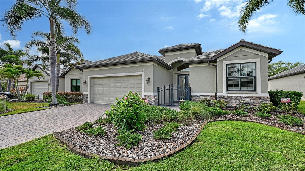 A single-story house with a beige stucco exterior, stone accents, and a paved driveway — 7702 RIO BELLA PLACE, BRADENTON, FL