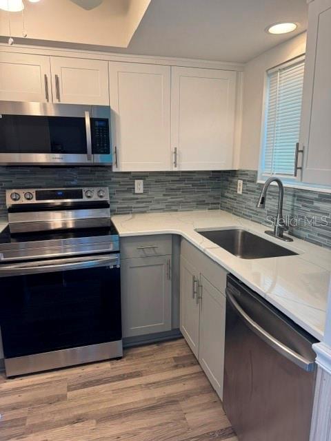 A modern kitchen features white cabinets, stainless steel appliances, gray tile backsplash, and light wood flooring — 801 83RD AVENUE N UNIT 310, ST PETERSBURG, FL