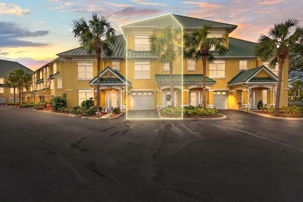 A three-story yellow townhouse with a green metal roof and a highlighted garage entrance — 6319 SUNSET BAY CIRCLE, APOLLO BEACH, FL