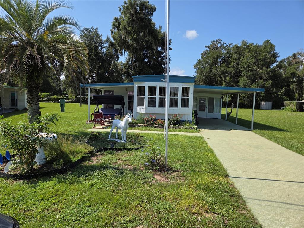 A single-story manufactured home with a carport, a white horse statue, and a palm tree — 10228 SE 24TH STREET, WEBSTER, FL