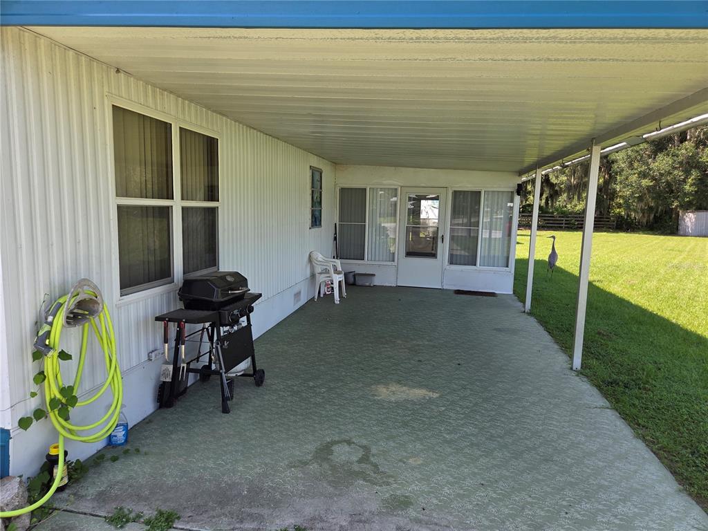 A covered concrete patio features a grill, a hose, and a view of a grassy yard — 10228 SE 24TH STREET, WEBSTER, FL