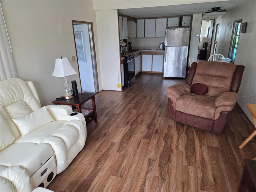 A living room features wood-look flooring, a ceiling fan, and large windows with vertical blinds — 10228 SE 24TH STREET, WEBSTER, FL