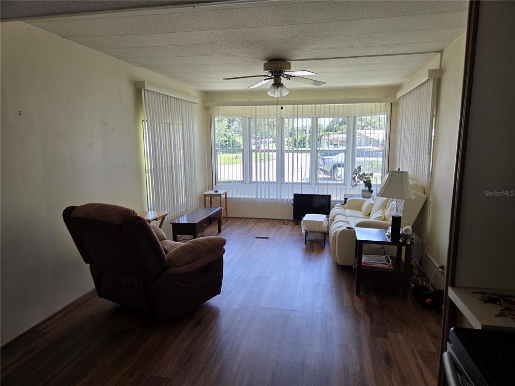 A living room features wood-look flooring, a ceiling fan, and large windows with vertical blinds — 10228 SE 24TH STREET, WEBSTER, FL