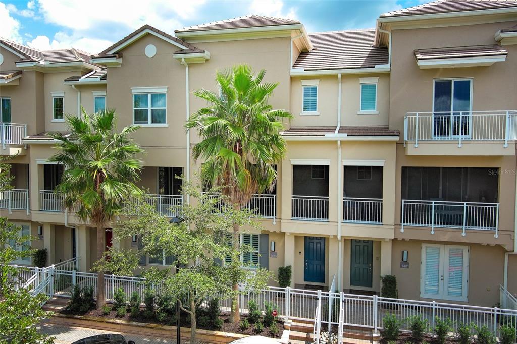 A row of three-story townhomes with beige stucco facades, balconies, and palm trees in front — 1465 LAKE GEORGE DRIVE, LAKE MARY, FL
