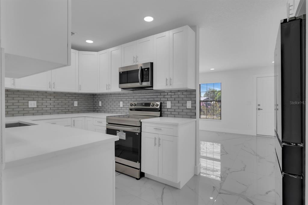 A modern kitchen features white cabinets, stainless steel appliances, and a gray subway tile backsplash — 2322 VINCENT ROAD, ORLANDO, FL