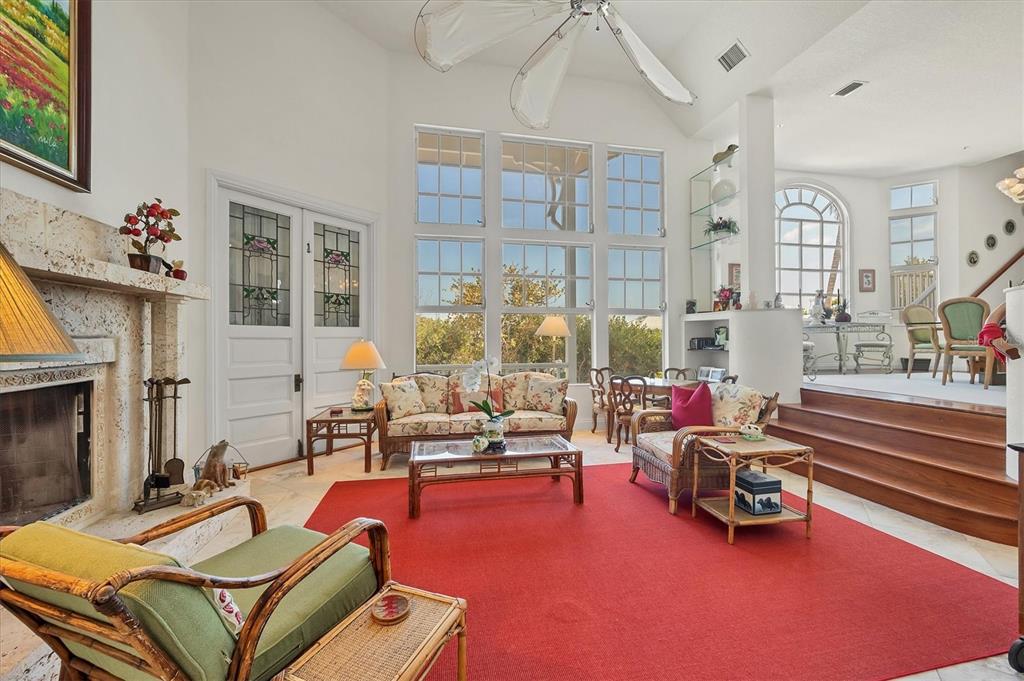 A sunlit living room features a stone fireplace, large windows, and a raised dining area — 1660 16TH STREET E, BOCA GRANDE, FL