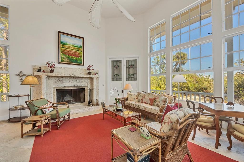 A living room features a stone fireplace, wicker furniture, a red rug, and large windows — 1660 16TH STREET E, BOCA GRANDE, FL