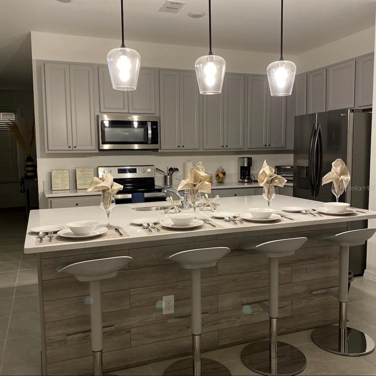 A kitchen features gray cabinets, a large island with bar seating, and stainless steel appliances — 1546 DISCOVERY STREET, DAVENPORT, FL