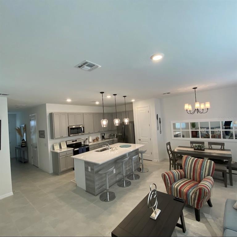 An open-concept kitchen features a central island with bar seating, gray cabinetry, and dining area — 1546 DISCOVERY STREET, DAVENPORT, FL