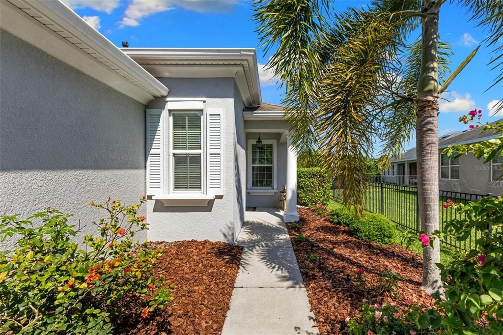 A concrete walkway leads to the front entrance of a gray house with white shutters — 6918 MAKERS WAY, APOLLO BEACH, FL