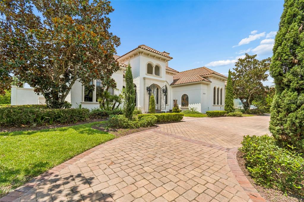 A white Mediterranean-style house features a tiled roof and a paved brick driveway — 13250 BELLARIA CIRCLE, WINDERMERE, FL