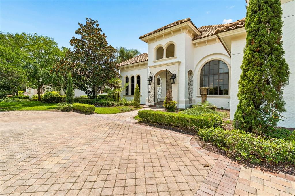 A paved driveway leads to the arched entryway of a Mediterranean-style home with stucco walls — 13250 BELLARIA CIRCLE, WINDERMERE, FL
