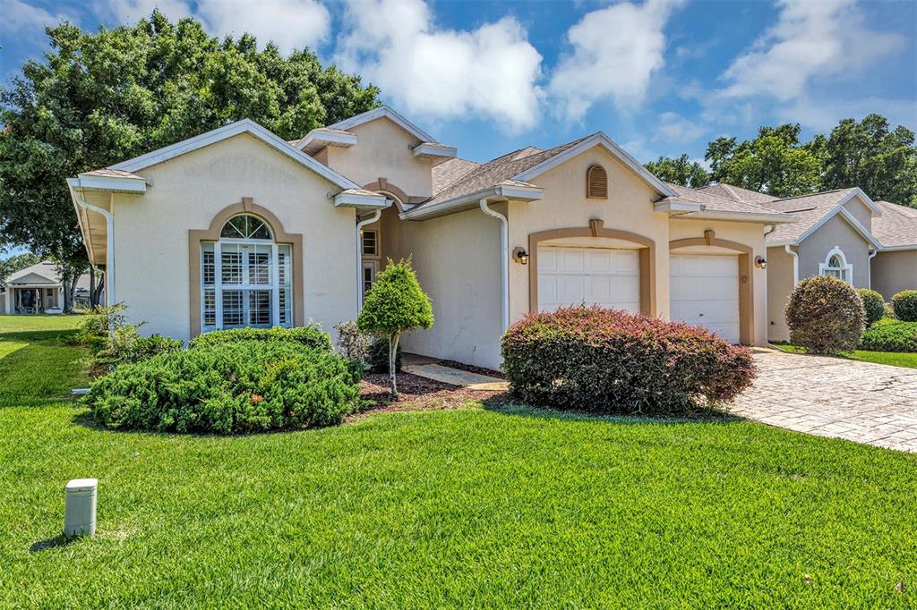 A single-story house with a beige stucco exterior, a two-car garage, and a landscaped lawn — 11003 SW 69TH CIRCLE, OCALA, FL