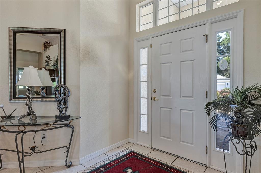 An entryway features a white front door with sidelights, a glass console table, and tile flooring — 11003 SW 69TH CIRCLE, OCALA, FL