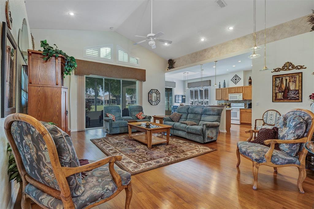 A living room with hardwood floors, vaulted ceilings, and an open view into the kitchen — 11003 SW 69TH CIRCLE, OCALA, FL
