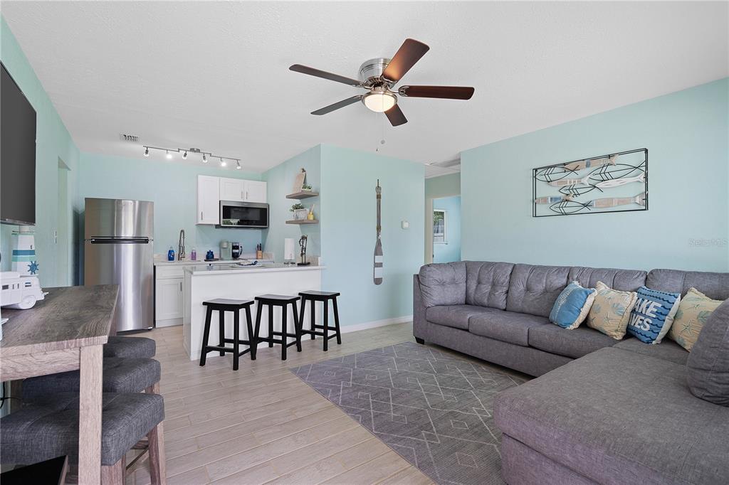 A living room and kitchen area feature light blue walls, gray tile flooring, and a sectional sofa — 6761 HIBISCUS AVENUE S, SOUTH PASADENA, FL