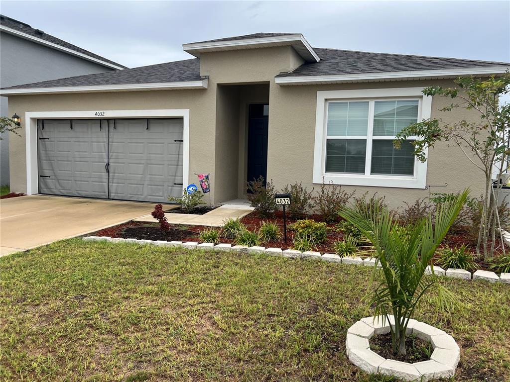A single-story house with a beige stucco exterior, a gray garage door, and front landscaping — 4032 GREY HERON LOOP, BARTOW, FL