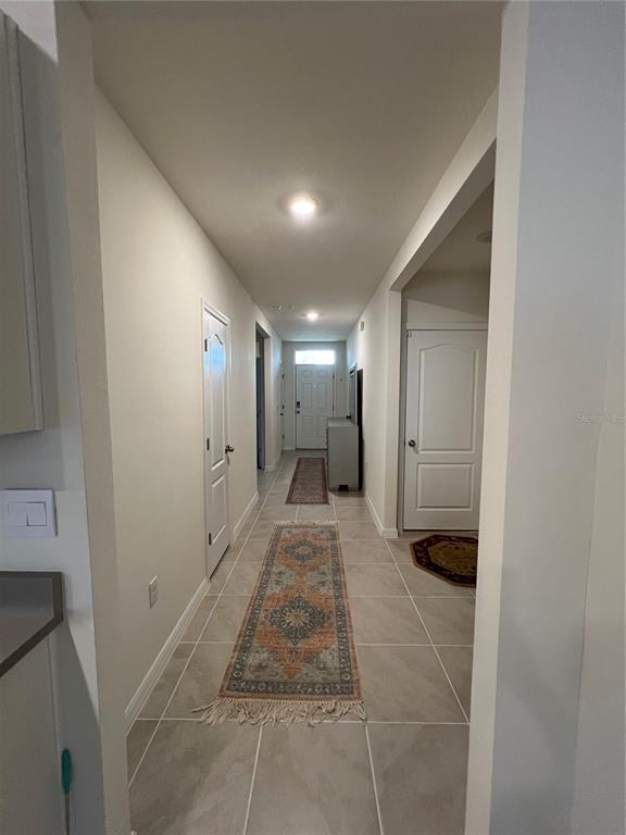 A tiled hallway leads to a front door, featuring two runner rugs and white doors — 4032 GREY HERON LOOP, BARTOW, FL