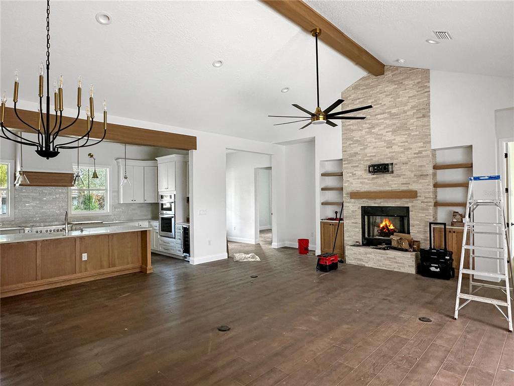 An open-concept living room and kitchen featuring a stone fireplace, wood beams, and hardwood floors — 935 N THOMPSON ROAD, APOPKA, FL
