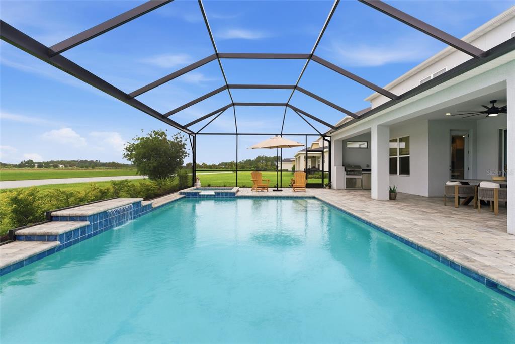 A swimming pool with a waterfall feature sits inside a screened lanai with patio furniture — 33774 CASTAWAY LOOP, WESLEY CHAPEL, FL