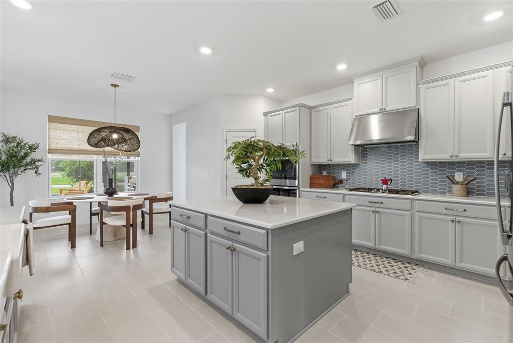 A kitchen features a gray island, light cabinetry, a blue tiled backsplash, and an adjacent dining area — 33774 CASTAWAY LOOP, WESLEY CHAPEL, FL