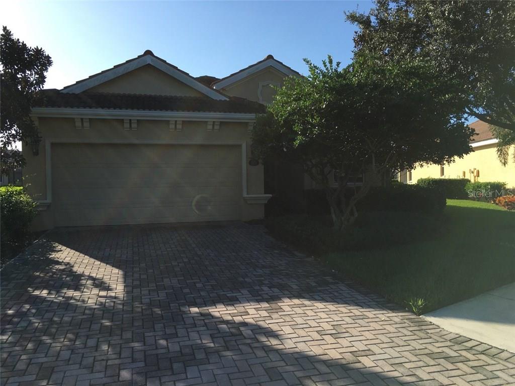 A single-story house with a beige stucco exterior, a two-car garage, and a paver driveway — 115 RIVER ENCLAVE CT. COURT, BRADENTON, FL